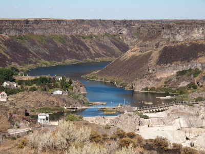 [At the foot of the canyon walls hundreds of feet high flows the wide Snake River. In this area it curves sharply before reaching the dam in the foreground of the photo.]